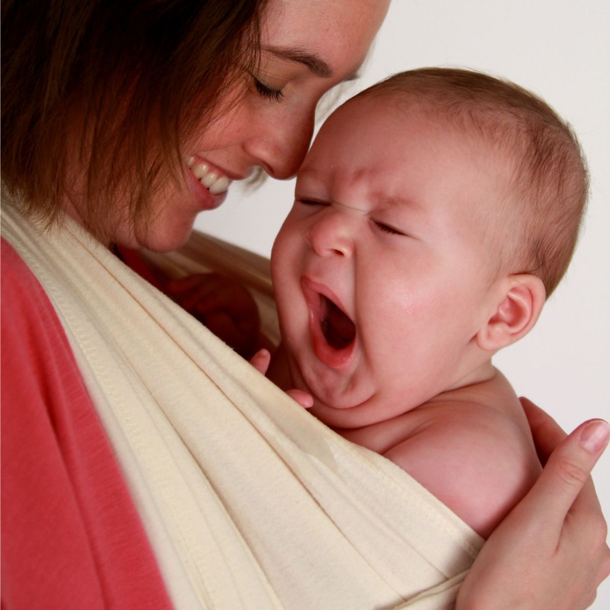 Yawning baby in a wrap on his smiling mom's chest