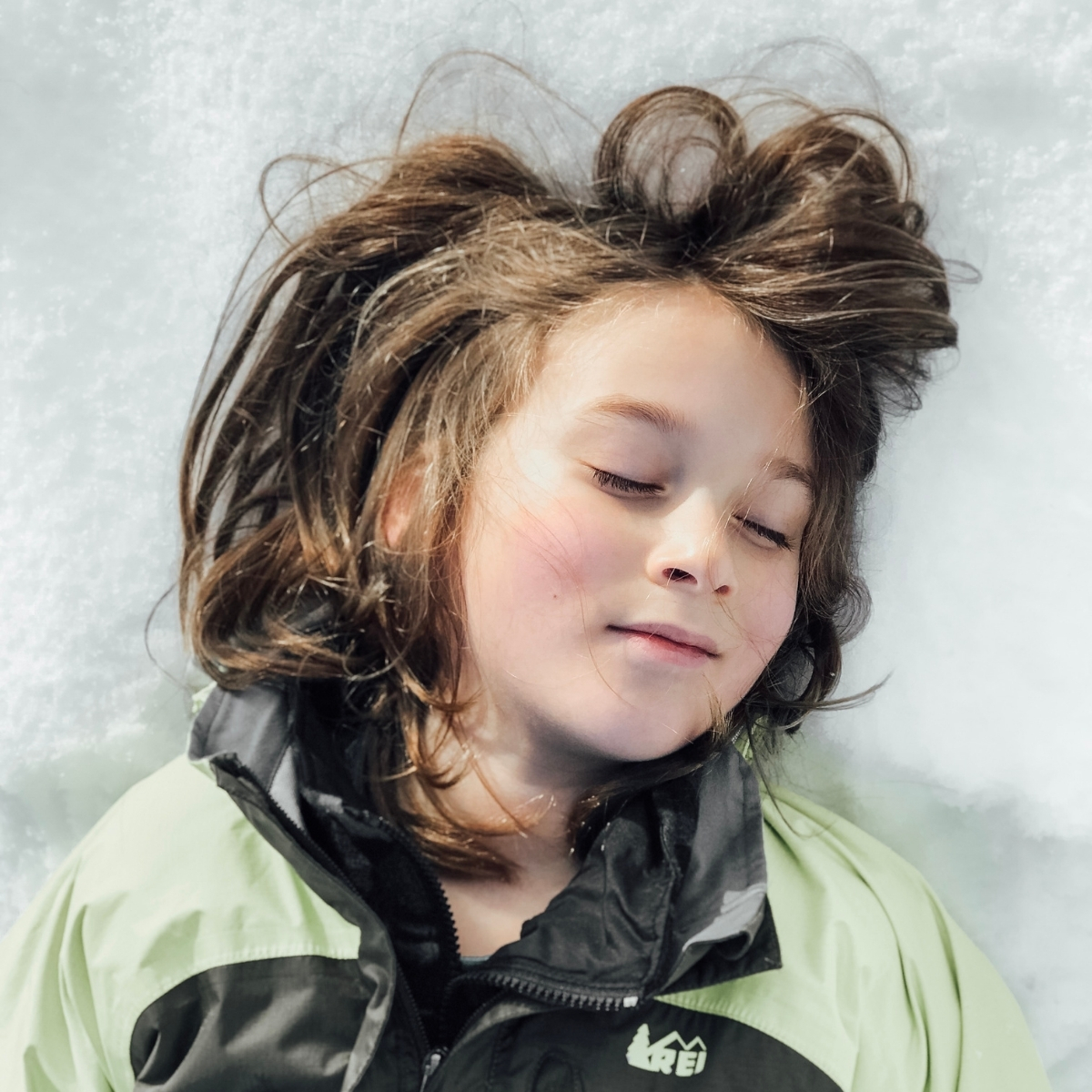 wildschooling boy lays blissfully in the snow in his winter gear on a nature adventure